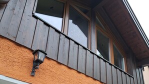 Un edificio con balcón de madera, una puerta y una ventana con una caja de metal adherida a la pared.