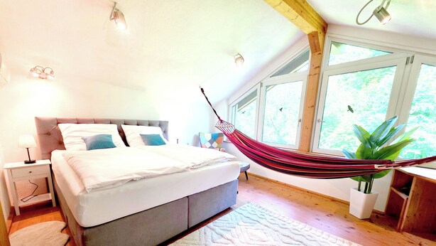 Un dormitorio con cama, mesita de noche, lámpara y una hamaca.