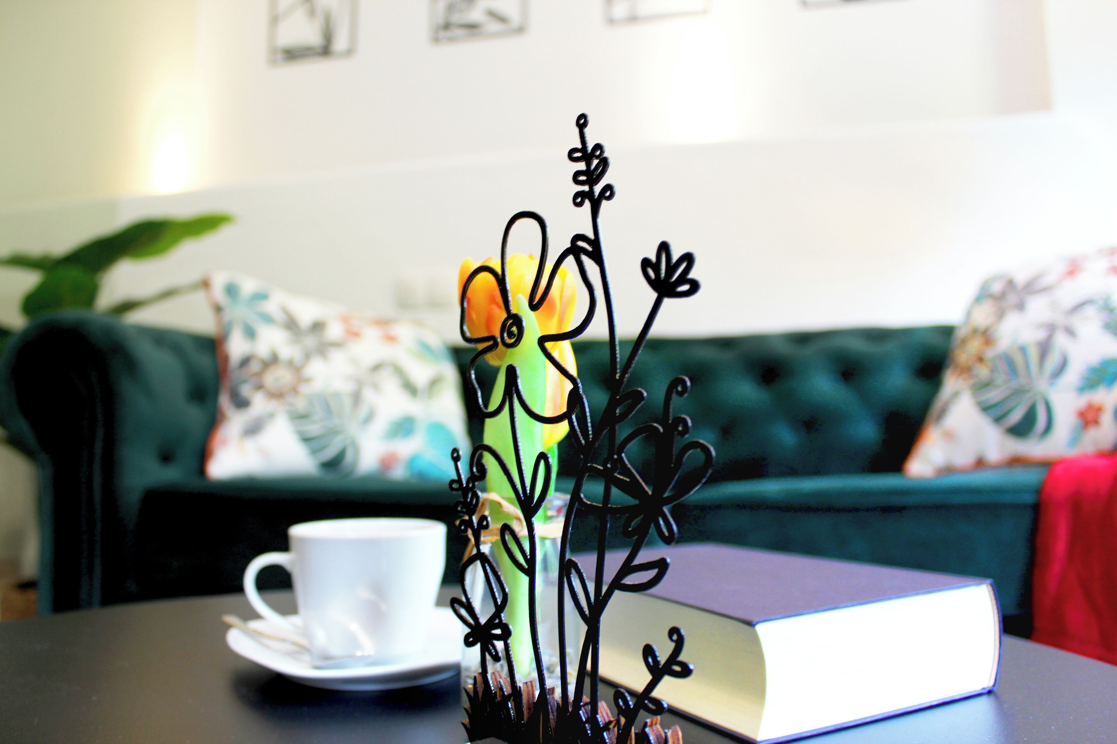 Een kamer met een groene bank, een witte beker op een schoteltje, en een boek op een tafel.