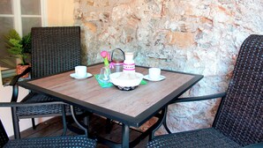 Mesa para dos con un fondo de pared de piedra, sillas de mimbre y una planta en maceta.