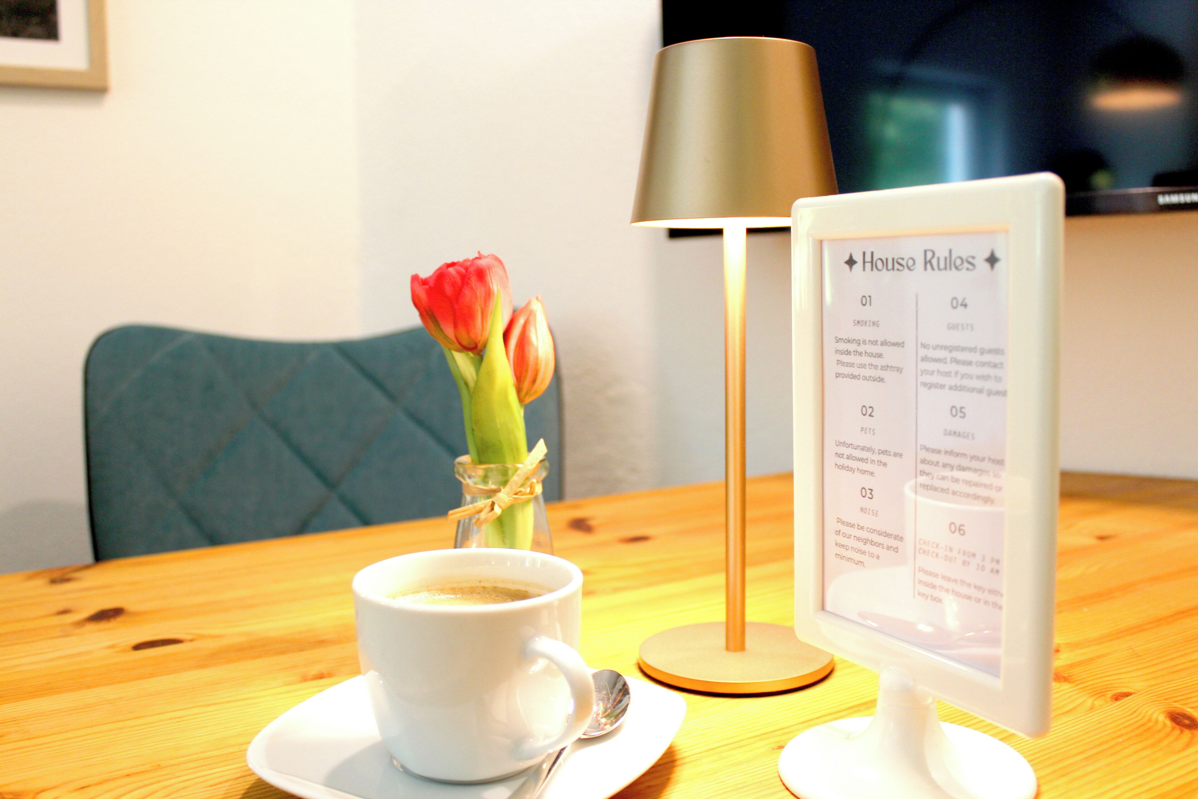 A table with a cup of coffee, a vase with a tulip, and a sign listing house rules.