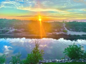 A calm lake with a sunset reflection, surrounded by greenery and rocks.