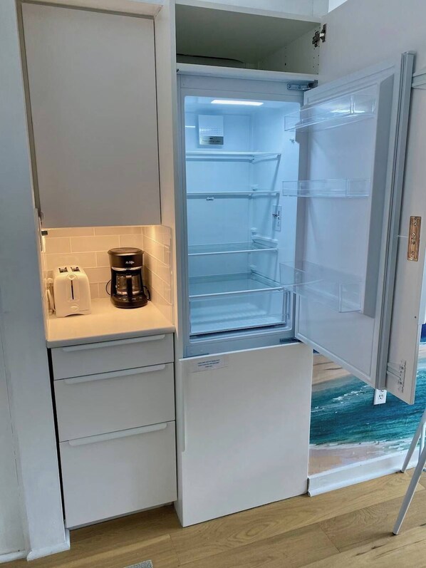 A compact kitchen with a built-in refrigerator, a coffee maker, and a toaster.