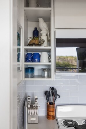 A kitchen with white cabinets, a stove, and various utensils. - GOOD VIBES LAKEFRONT CONDO (Glen Arbor)