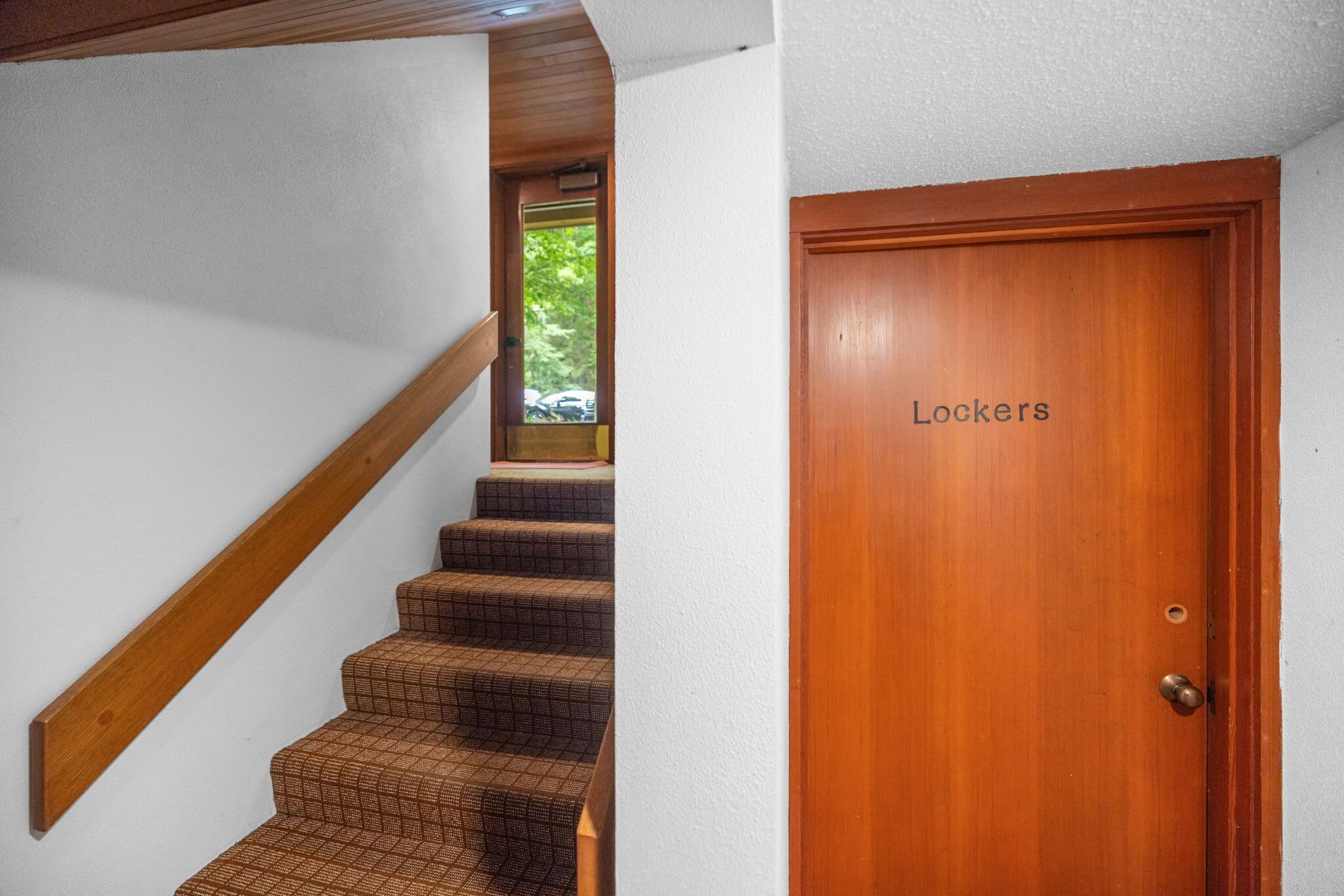 A staircase with a wooden handrail leading to a door labeled 'Lockers'.