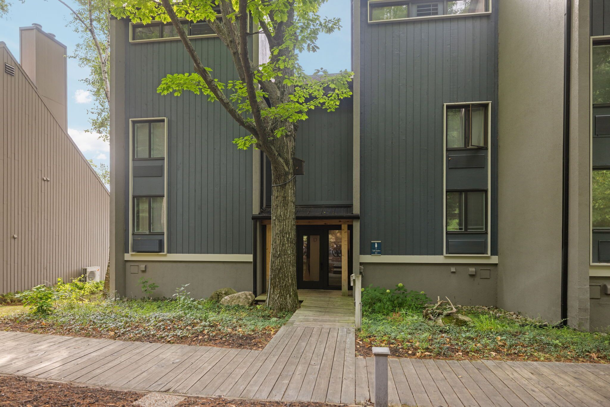 A modern building with a central tree, a wooden pathway, and a sign indicating a toilet.