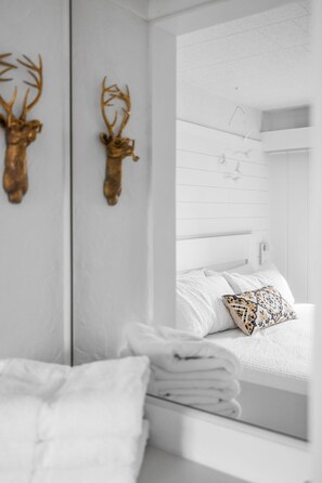 A white room with a bed, a mirror, and two deer antlers on the wall.