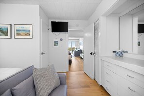 A modern interior with a grey sofa, a flat-screen TV mounted on the wall, and a wooden floor. - GOOD VIBES LAKEFRONT CONDO (Glen Arbor)