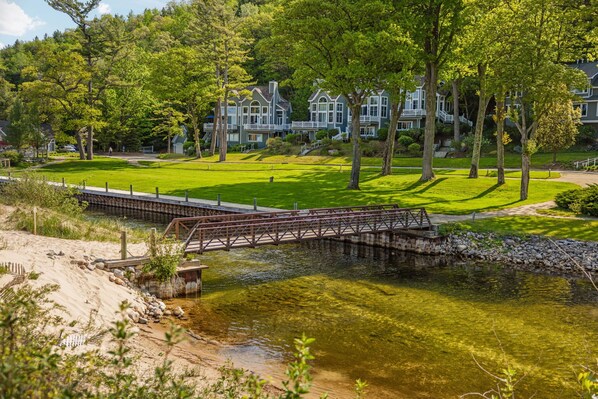 A residential area with a bridge over a water body, surrounded by lush greenery and a row of houses.