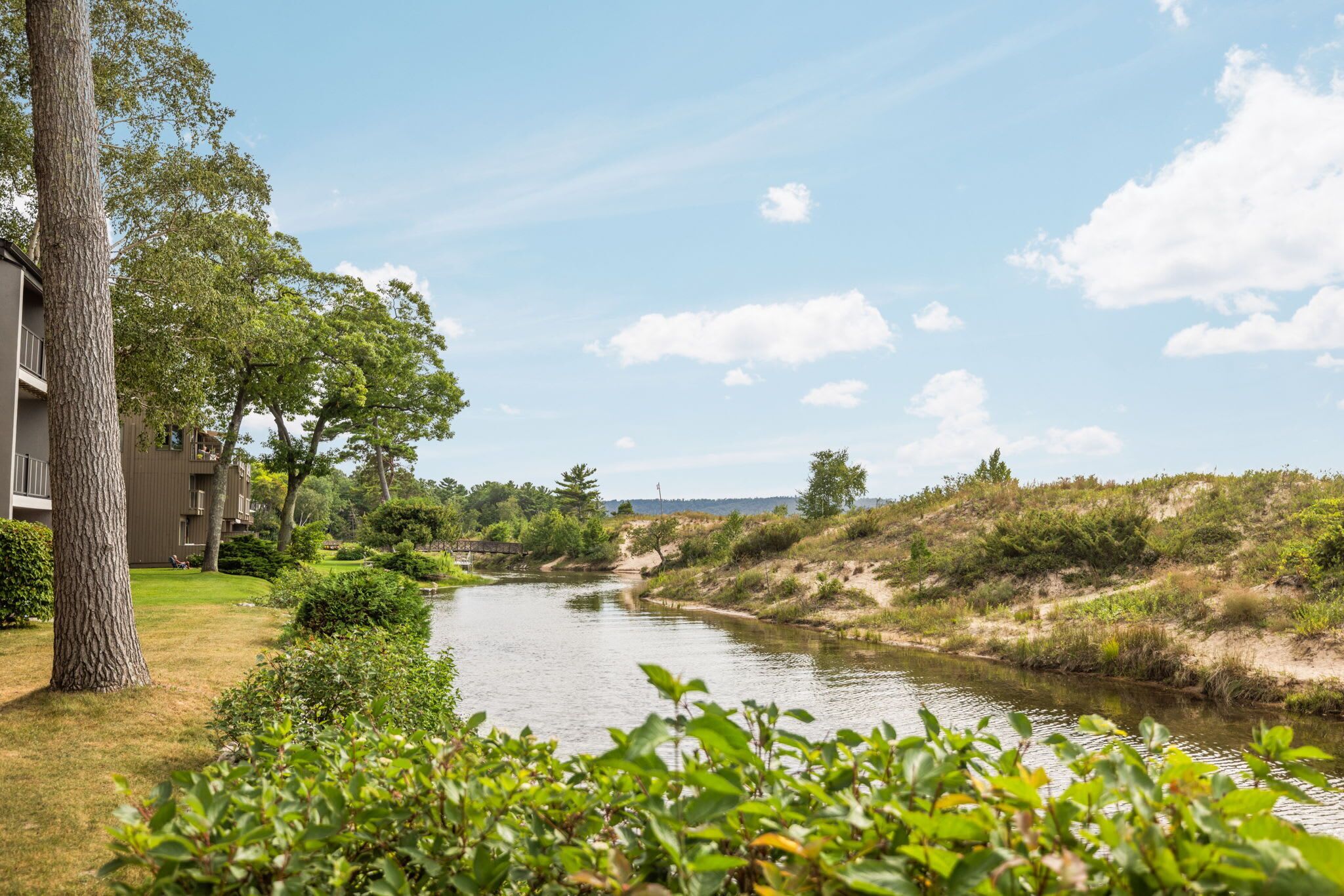 A river flowing through a landscaped area with trees and a building on the left.