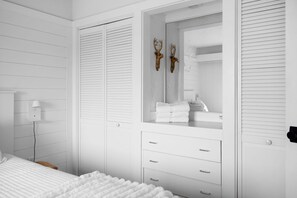 A bedroom with a bed, a bedside table, a lamp, a wardrobe with a mirror, and a small shelf with towels.