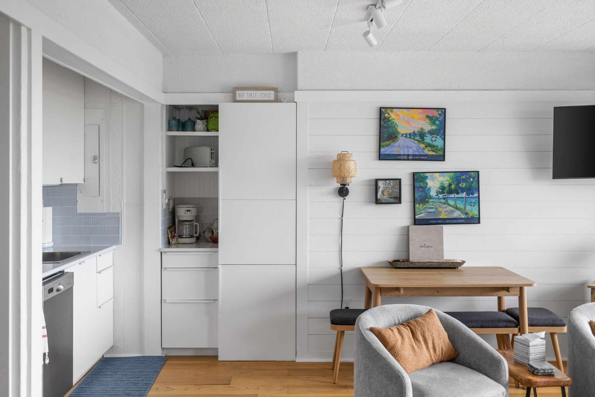A modern kitchen with white cabinetry, a coffee machine, and a dining area with a table and chairs.
