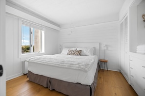 A bedroom with a large bed, a window, a bedside table, and a wardrobe.