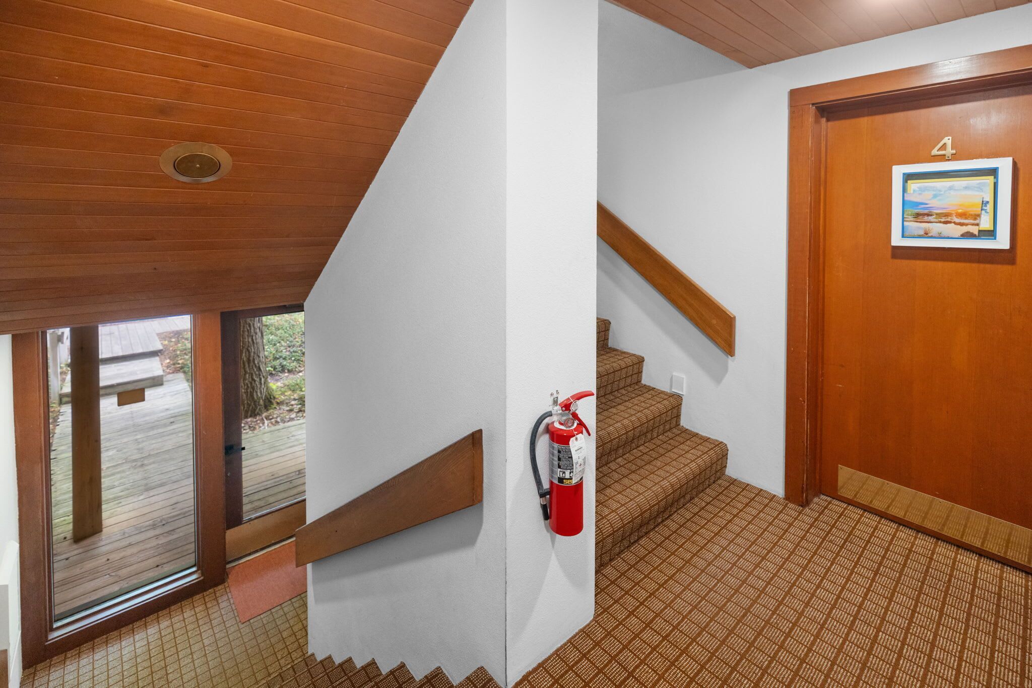 Un escalier, un extincteur fixé au mur, une porte en bois portant le numéro 4 et une fenêtre donnant sur l’extérieur.