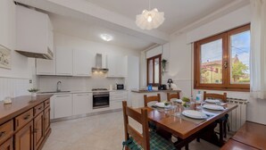 A modern kitchen with white cabinets, a dining table set for four, and a large window with a view of the outside. - Marco Polo Airport GATE 2 Comfy 1+1BR Apt with Venice Access (Venezia)