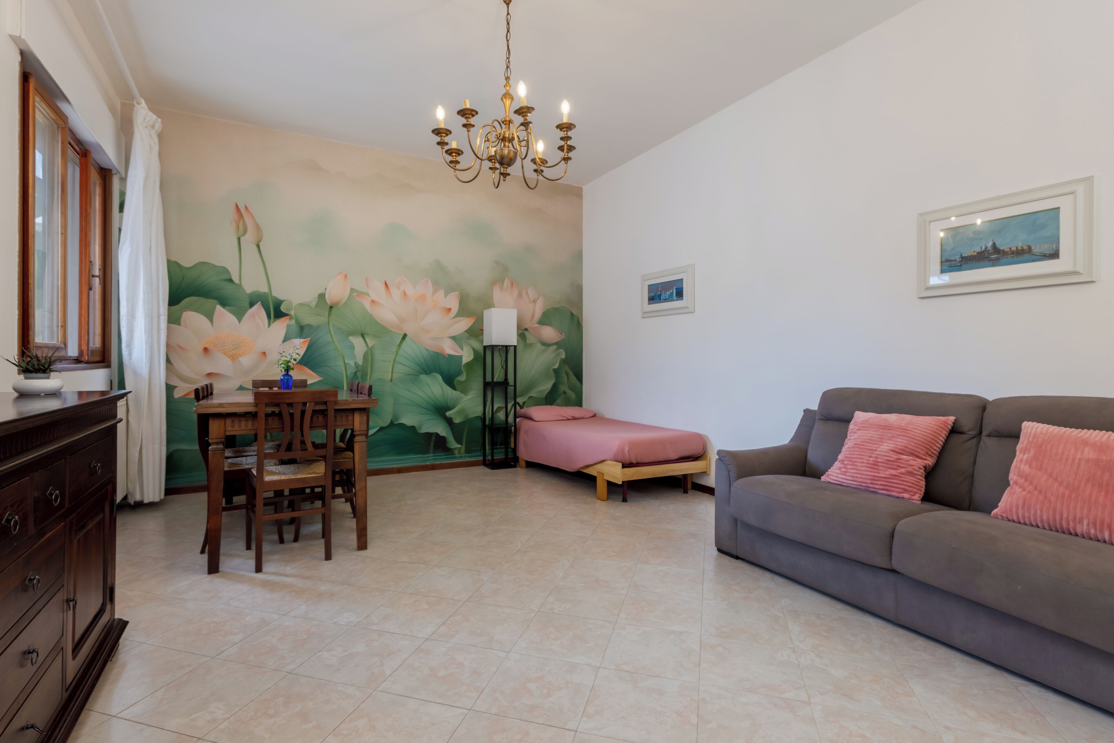 Un salon agrémenté d’une grande fresque florale, d’un lustre, d’un canapé, d’un lit et d’un coin repas.