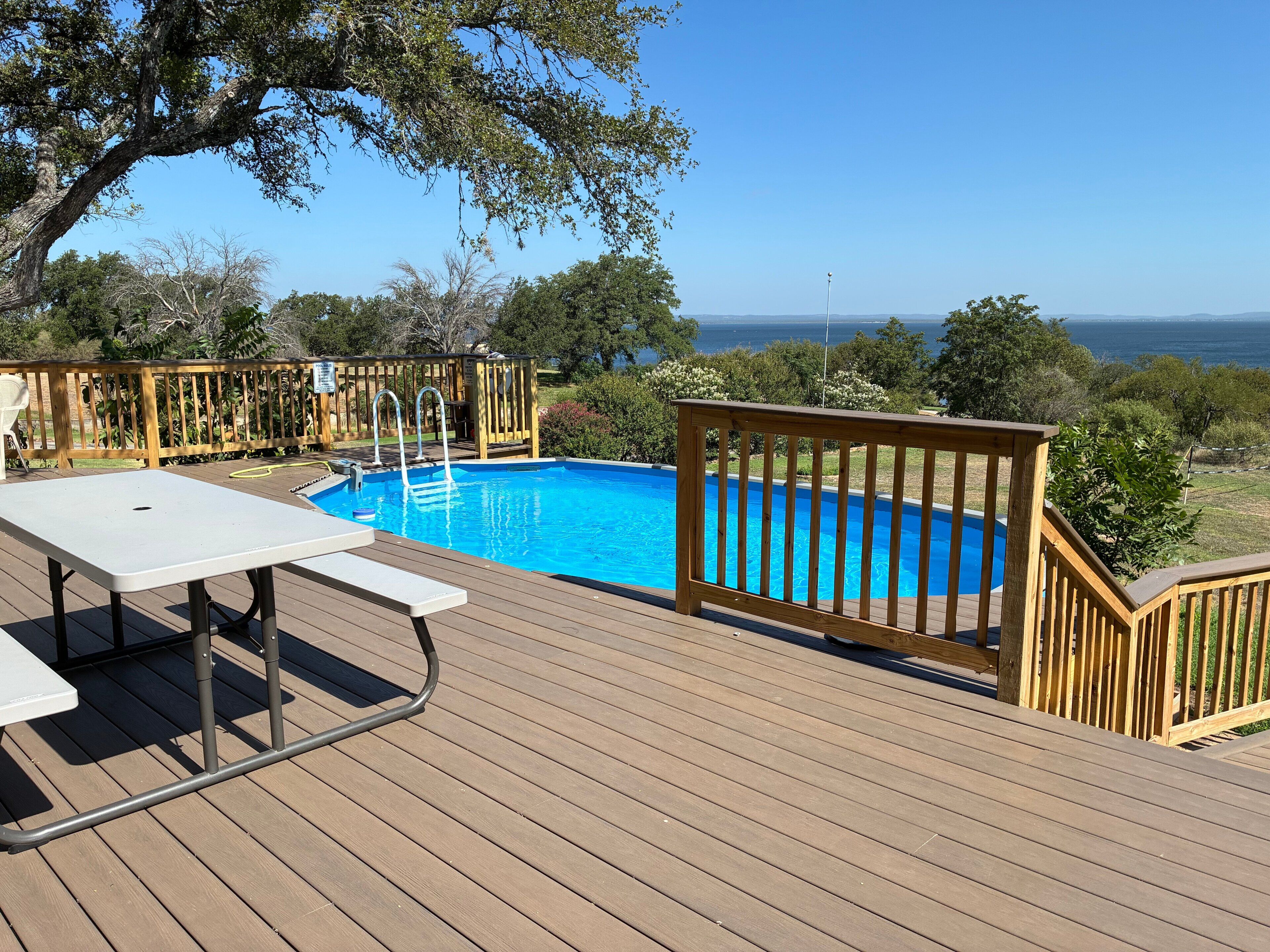 Eine Holzterrasse mit Pool, Tisch und Blick auf den Ozean.