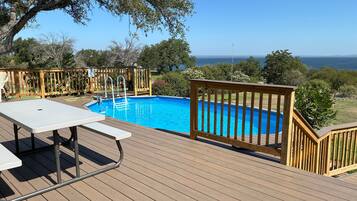 Eine Holzterrasse mit Pool, Tisch und Blick auf den Ozean.