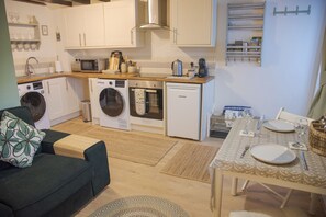 A compact kitchen with a washing machine, microwave, oven, and a dining area with a table set for two. - Little Thornsett (Buxton)