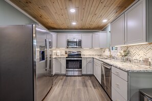 A modern kitchen with stainless steel appliances, wooden ceiling, and herringbone patterned backsplash. - Rustic Escape:Indoor Pool|Hot Tub|WiFi|8 Min to PF (Sevierville)