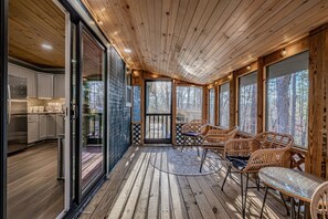 A wooden deck with wicker furniture and glass doors leading to a kitchen. - Rustic Escape:Indoor Pool|Hot Tub|WiFi|8 Min to PF (Sevierville)