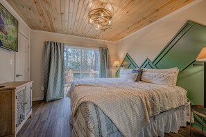 A bedroom with a wooden ceiling, a large bed with patterned bedding, a green accent wall, and a window with curtains. - Rustic Escape:Indoor Pool|Hot Tub|WiFi|8 Min to PF (Sevierville)