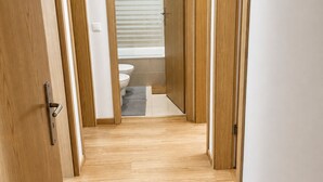 A hallway with wooden flooring leading to a bathroom with a toilet and a window with blinds. - Room-charming Lisbon Apartment in Quiet (Lisbon)