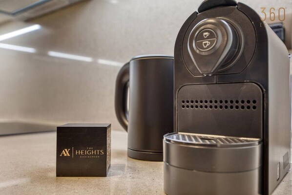 Une machine à café, une boîte étiquetée « AX Heights Residences », et une tasse sur un comptoir.