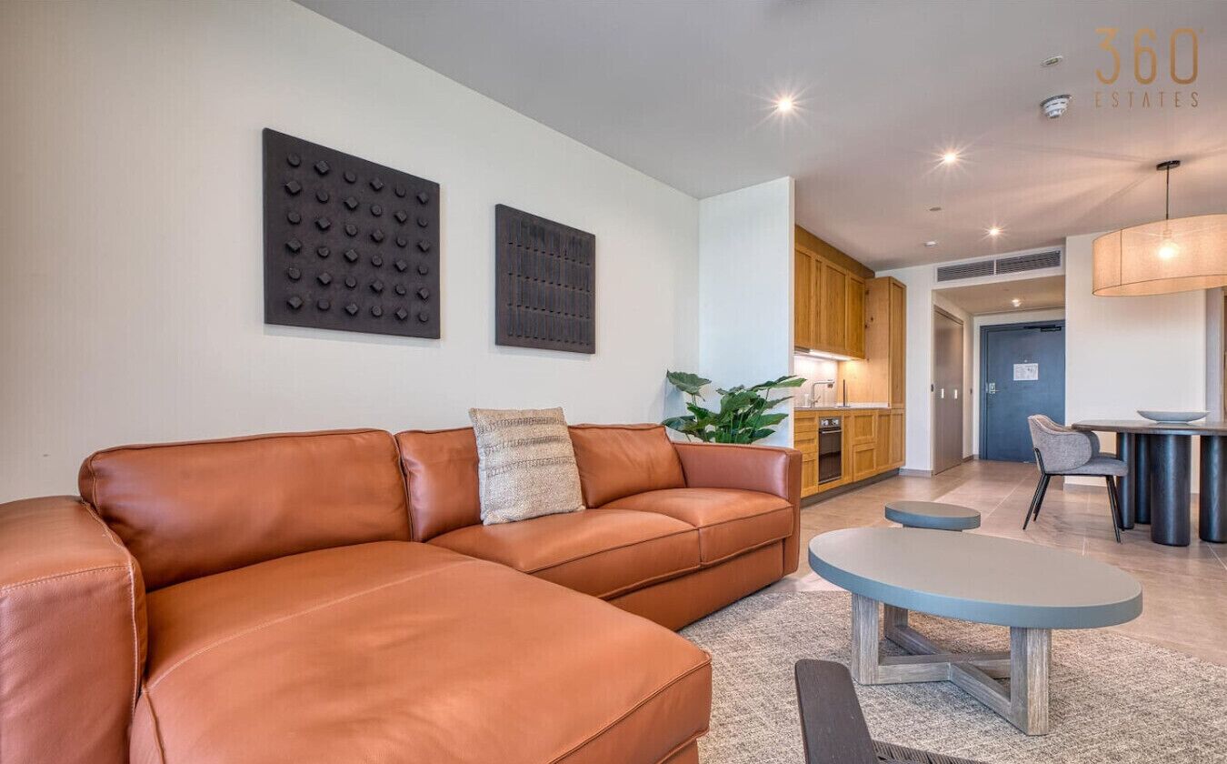A modern living room with a leather sofa, a round coffee table, and a dining area with a table and chairs.