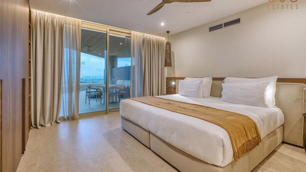A hotel room with a large bed, a ceiling fan, and a view of the ocean through a sliding glass door. - Unwind in Style, Luxury Apartment w/ Scenic Views (Rabat)