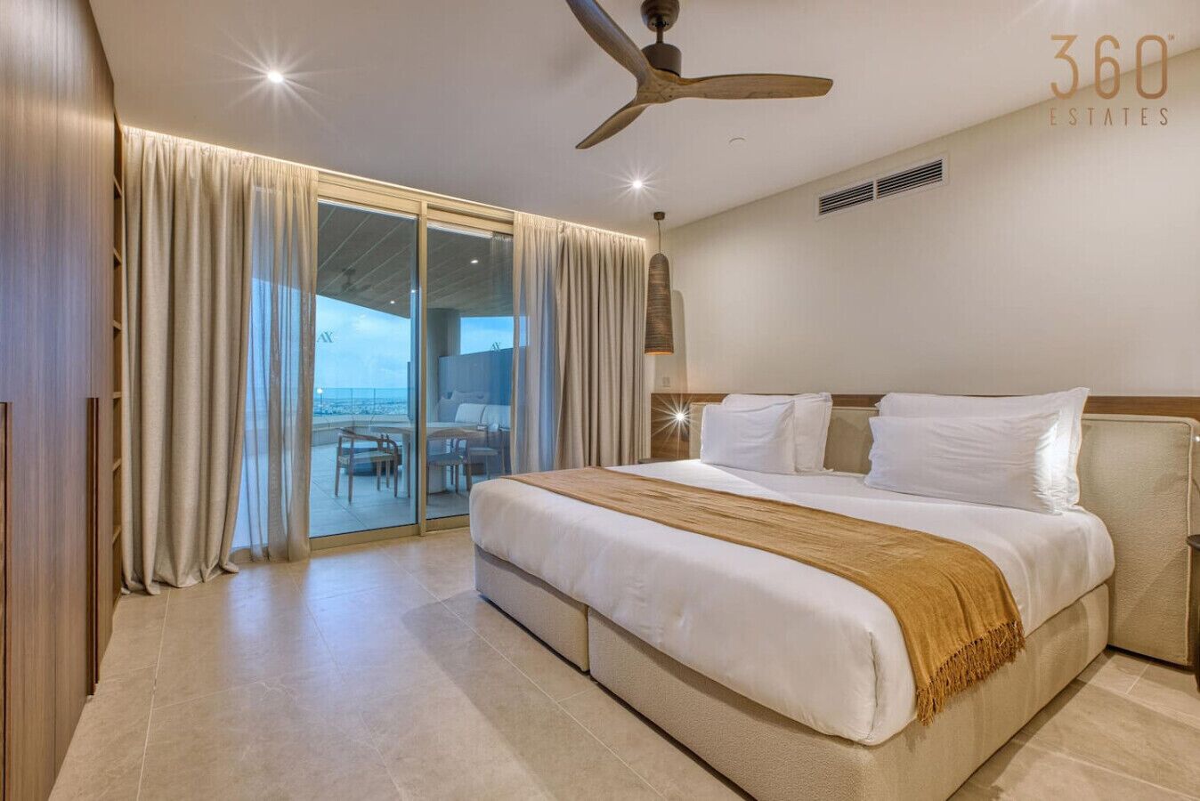 Habitación de hotel con una cama grande, ventilador de techo y vista al océano a través de un ventanal corredero.