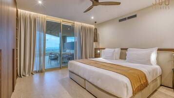 Habitación de hotel con una cama grande, ventilador de techo y vista al océano a través de un ventanal corredero.