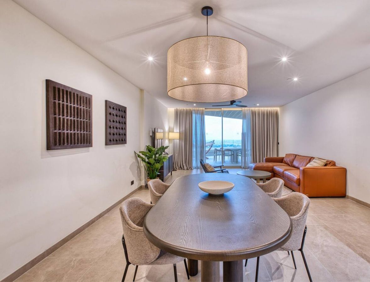 Un espace de repas moderne avec une table ronde, des chaises, un luminaire suspendu et une vue sur l’océan grâce à de grandes fenêtres.