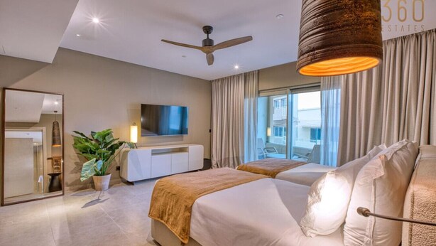 Een moderne hotelkamer met een groot bed, een televisie, een plafondventilator en uitzicht naar buiten.