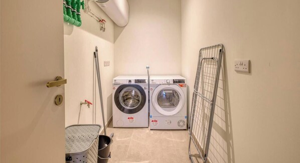 A laundry room with two washing machines, a drying rack, and a metal bucket. - Rabat Luxe Apartment with outdoor Terrace & Views! (Rabat)