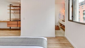 A modern bedroom with a bed, a wooden desk, a built-in wardrobe, and a window with a view of buildings. - w Beautiful 1BR Retreat in Vibrant Zona T (Bogotá)