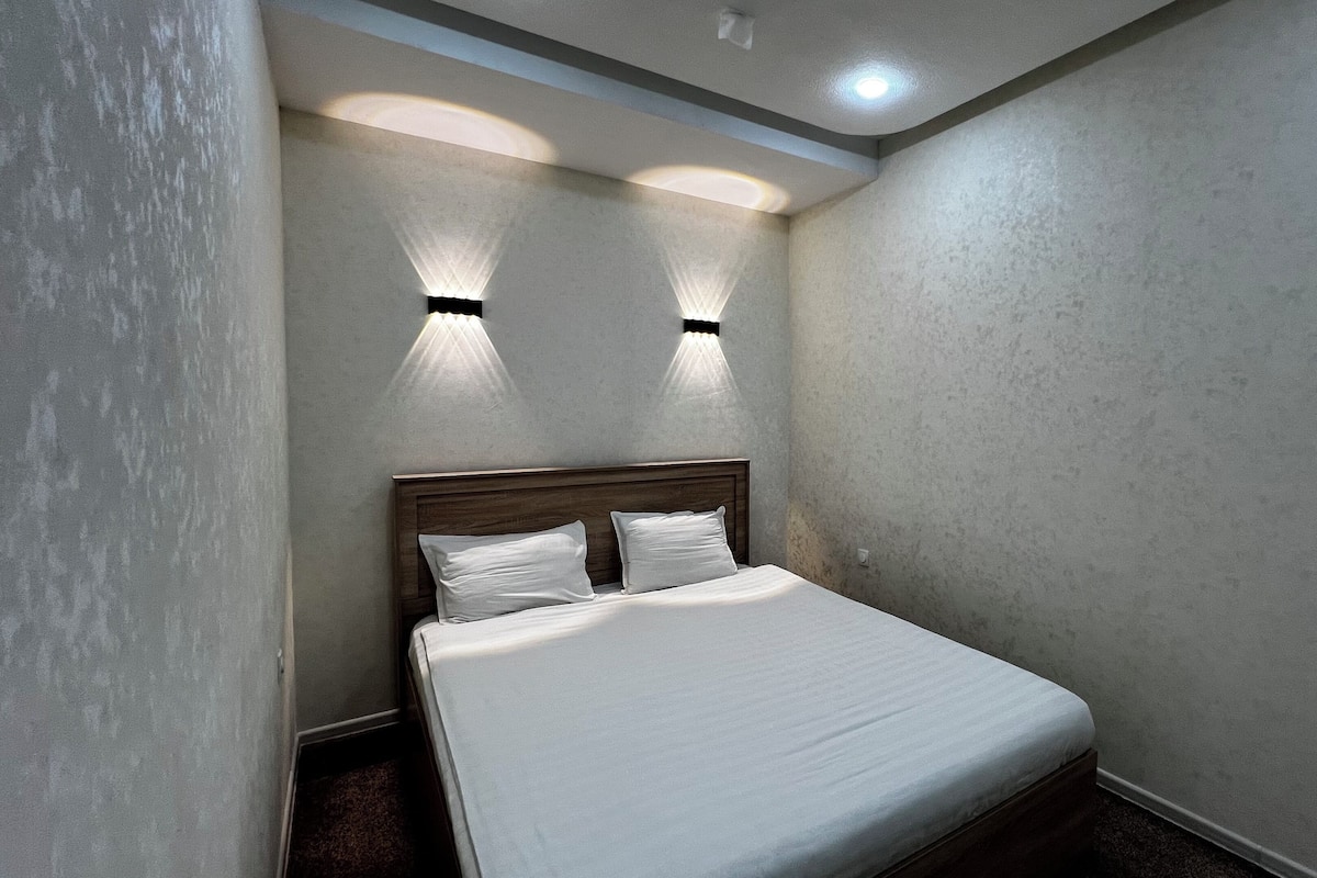 A single bed with a wooden headboard, two wall-mounted lights, and a textured wall.