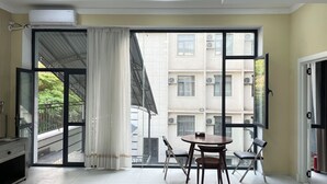 A room with a large sliding glass door leading to a balcony, a round table with two chairs, and a built-in air conditioning unit on the wall. - Chinor Hotel Fergana (Fergana)
