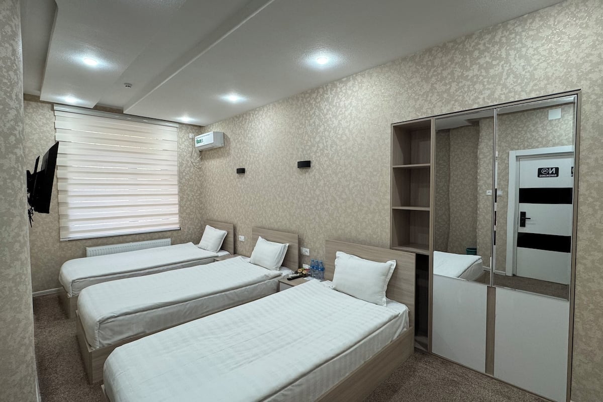A hotel room with three single beds, a wardrobe, a mirror, and a television mounted on the wall.
