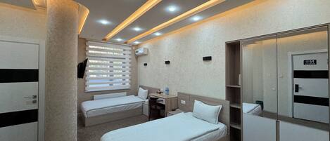 A hotel room with two single beds, a desk, a chair, a wardrobe, and a large pillar.