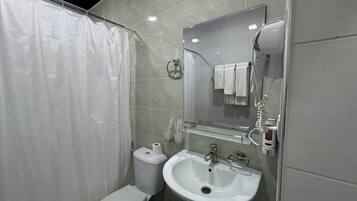 Un baño moderno con ducha, inodoro, lavamanos y espejo con toallero.