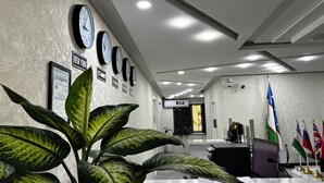 A reception area with multiple clocks, flags, and a plant. - Chinor Hotel Fergana (Fergana)