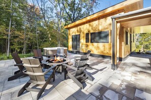 An outdoor patio with a fire pit, seating, and a wooden building with large windows. - Luxury Barn | Theater & Basketball Court (Winhall)