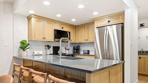 A modern kitchen with wooden cabinets, stainless steel appliances, and a central island with bar stools. - Giant Steps 30 Ski in/Ski out (Brian Head)