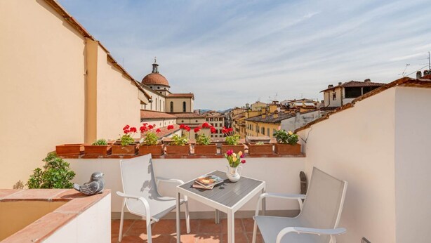 A terrace with a table and chairs, a pigeon statue, and potted plants with flowers. - Apartments Florence - Blumberg (Firenze)