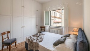 A bedroom with a bed, a chair, a window with a view, and a radiator. - Apartments Florence - Blumberg (Firenze)