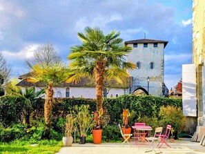 A courtyard with a stone building, palm trees, and a seating area with chairs and a table. - Beautiful Romantic Suite with private terrace (Vicq-d'Auribat)
