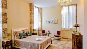 Quarto com cama, um candelabro, uma mesinha com um vaso e uma cadeira.