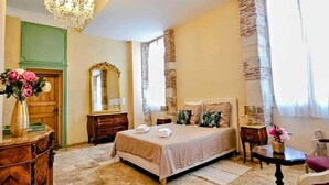 Quarto com uma cama grande, um candelabro, cômoda, espelho e janela com cortinas.