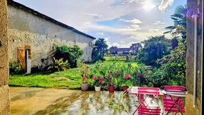 Um pátio com piso de concreto, um edifício rústico e um jardim com plantas em vasos e uma cadeira dobrável vermelha.